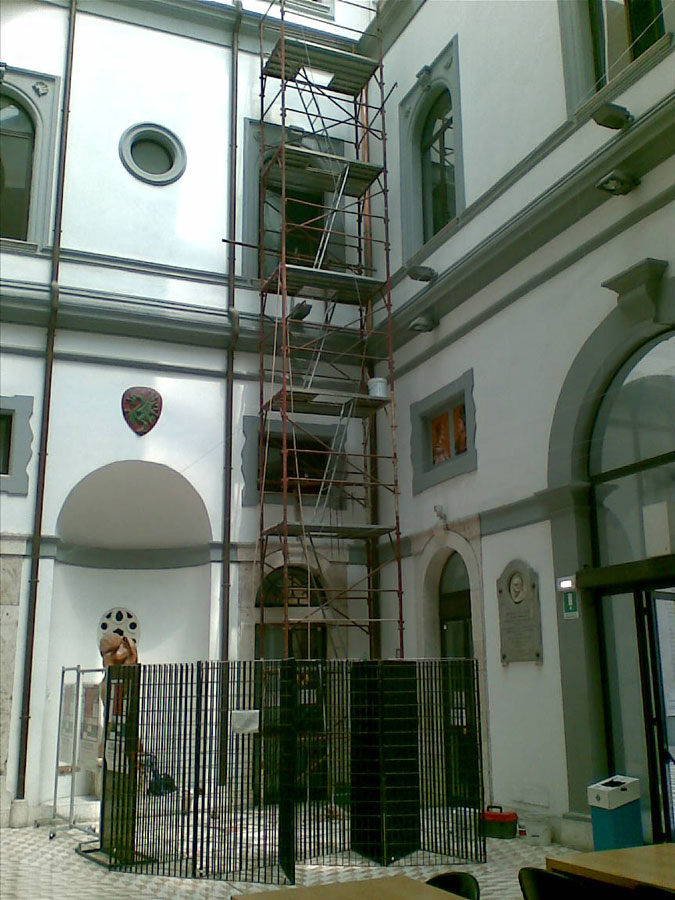 Ponteggio in tubi metallici rossi recintato da grate nere nel cortile interno di un edificio storico con facciate bianche
